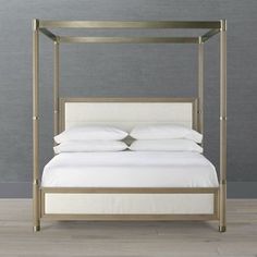 a four poster bed with white sheets and pillows on top of it, against a gray wall