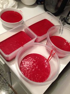 four plastic containers filled with red liquid on top of a stove