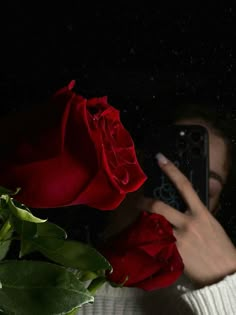 a woman taking a selfie with her cell phone next to a red rose in the dark