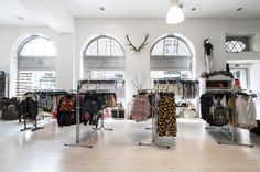 the inside of a clothing store with lots of clothes on racks and hanging items in front of large arched windows