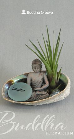 a small buddha statue sitting on top of a bowl filled with rocks and plants next to a plaque that says breathe