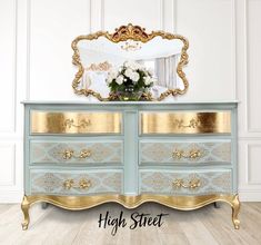 a blue dresser with gold trim and flowers on top