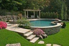 a pool surrounded by stone steps next to a lush green yard with flowers and trees