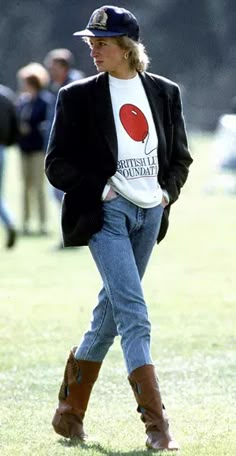 a woman walking in the grass wearing boots and a t - shirt with an image of a cherry on it