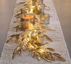 a long table with candles and gold leaves on the runner, along with silver cups