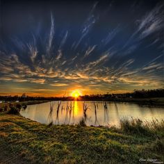 the sun setting over a body of water with trees in the foreground and clouds in the background