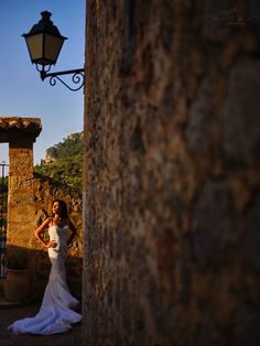 a woman in a wedding dress standing next to a stone wall with a light on it