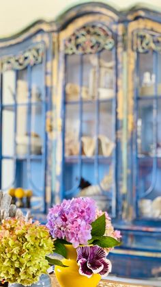 two vases filled with flowers sitting on top of a table next to a blue china cabinet