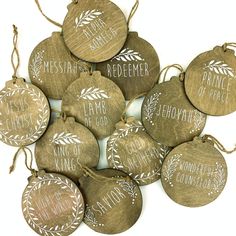 wooden ornaments with hand painted names and leaves are hanging from twine strings on a white background