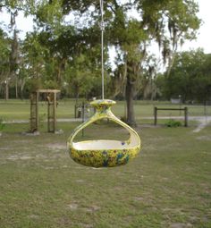 a bird feeder hanging from a tree in a park with lots of trees and grass