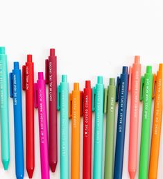 many different colored pens lined up on a white surface with words written in the middle