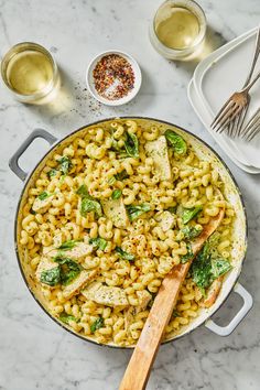 pasta with chicken and spinach in a skillet on a marble countertop next to silverware