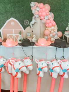 pink and white horse head candles are lined up on a table with balloons in the background