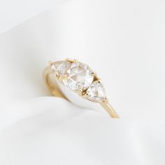 a yellow gold ring with three pear shaped diamonds on the top and bottom, sitting on a white cloth