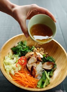 a person is pouring sauce into a bowl of food that includes chicken, lettuce and carrots