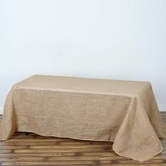 an empty table with a tan linen over it on wooden floor next to white wall