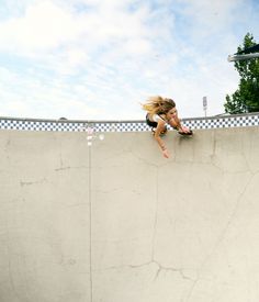 a woman riding a skateboard up the side of a cement wall at a skate park