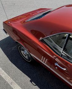 an old red car parked in a parking lot next to a curb with no one on it