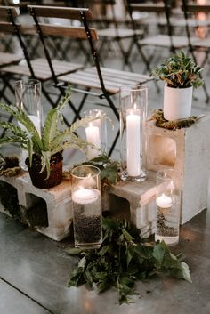 candles and plants are arranged on concrete blocks in front of a bench with metal chairs