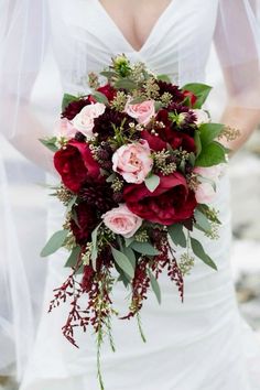 a bridal holding a bouquet of red and pink flowers with greenery on it