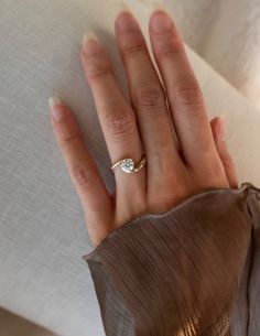 a woman's hand with a diamond ring on top of her left hand, resting against a white sheet