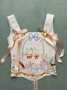 an embroidered apron with two cats and flowers on the front, tied in pink ribbon