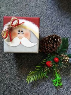 a christmas present sitting on the floor next to a pine cone with a santa clause painted on it