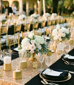 a long table is set up with black and white linens, silverware, and gold chargers