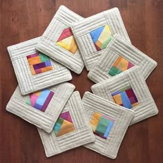 four quilted coasters with colorful squares on them sitting on a wooden table top