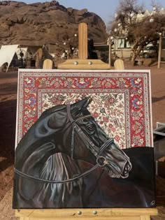 a painting of a black horse on an easel in front of some desert mountains