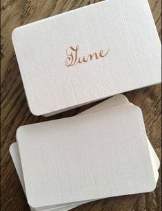 two white business cards sitting on top of a wooden table with the word june written in gold foil