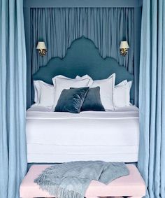 a bed with blue headboard and pillows in a room that has curtains on the wall