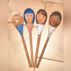 four wooden spoons with faces on them sitting next to each other in front of a tile wall