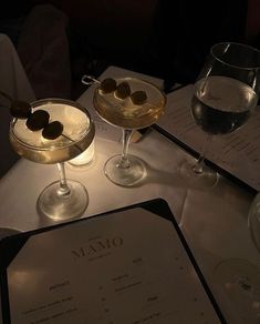 two martinis with olives sit on a table next to a menu and wine glasses