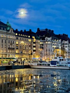 boats are docked in the water at night near some buildings and trees with lights on them