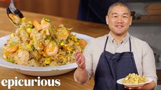 a man holding a plate of food next to a bowl of shrimp and rice on a table