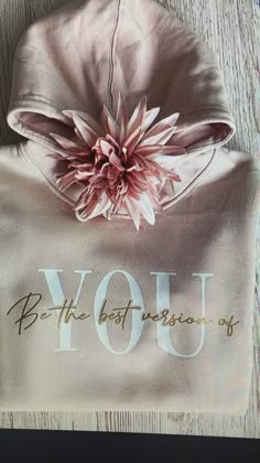 a pink flower on top of a white shirt with the words you be the best in front of it