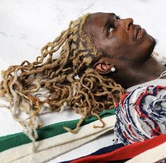 a man with dreadlocks laying on top of a blanket covered in scarves