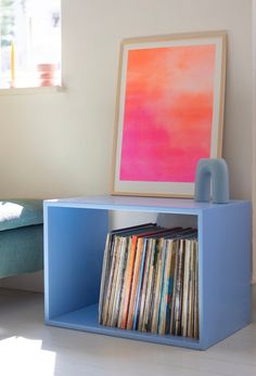 a blue shelf with records on it in front of a window and a painting behind it