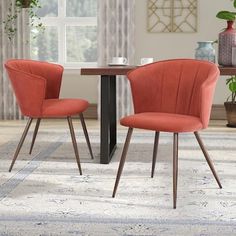 two orange chairs sitting at a table in front of a potted plant on a rug