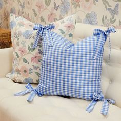 two blue and white pillows sitting on top of a couch next to a basket filled with flowers