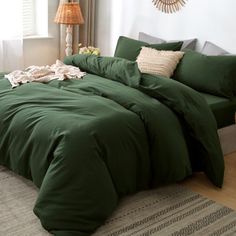 a bed with green comforter and pillows in a white room next to a window