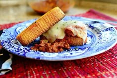 a blue and white plate topped with food on top of a red table cloth next to a fork