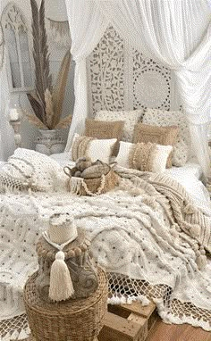 a white bed covered in lots of pillows and blankets next to a wicker basket