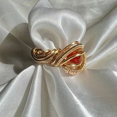 a gold ring sitting on top of a white satin fabric with an orange stone in the center