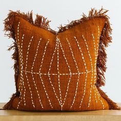 a brown and white decorative pillow with fringes on the front, sitting on a wooden table