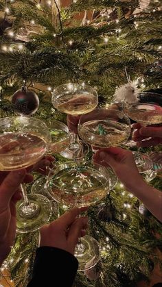 several people are holding wine glasses in front of a christmas tree with lights on it