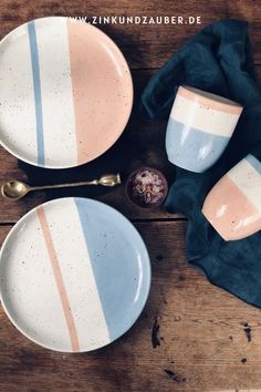 three plates and two cups on top of a wooden table next to a napkin with spoons