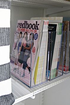 a shelf filled with magazines and books on top of white shelving unit shelves in a room