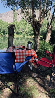 there is a picnic table with two chairs next to the water and trees in the background